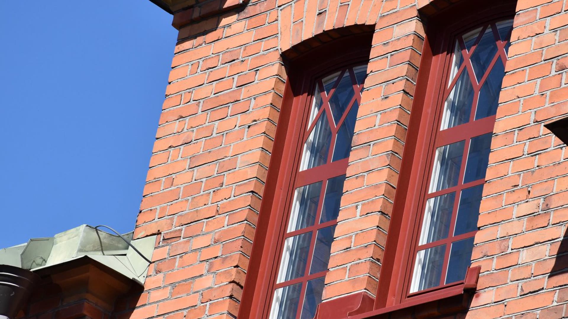 Två spröjsade fönster med mörkröda karmar i en tegelfasad